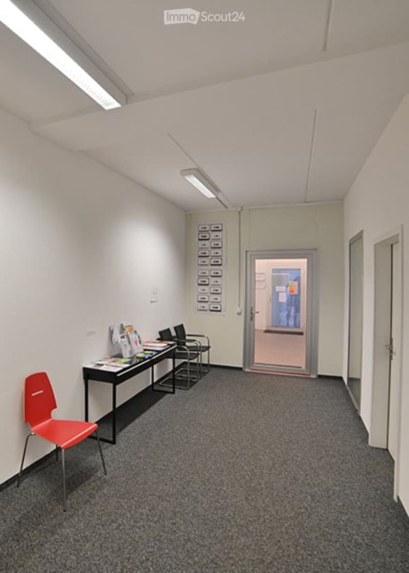 A small, well-lit room with a red chair, a black table, and a desk with chairs, likely used as a waiting or meeting area.