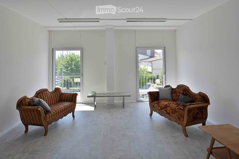 Bright living room with two sofas, a glass coffee table, and a wooden side table, featuring large windows and a view of greenery.
