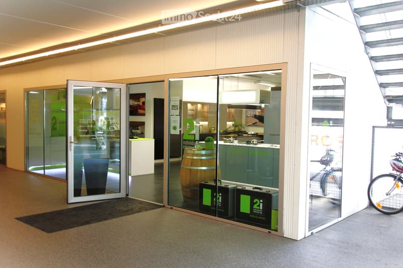 Modern office space with glass walls, barrel as a centerpiece, kitchen area with fridge, sink, and counter, and bicycles outside.