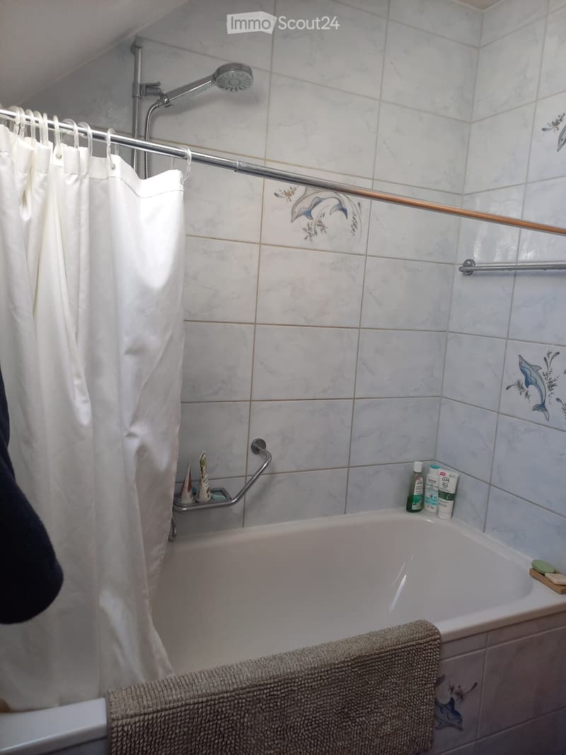 Bathtub with a white shower curtain, towel on the edge, and a shower rack with soap and bottles.