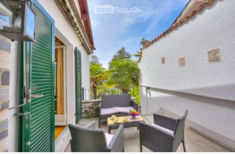 Balcony with outdoor furniture including a sofa, table, and chairs, overlooking a scenic view with palm trees.
