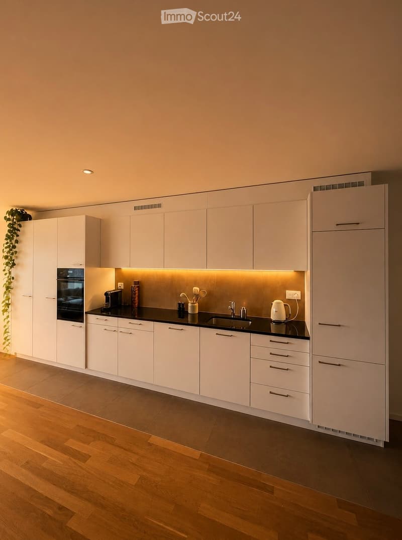Modern kitchen with white cabinets, black countertops, and wooden flooring. Features include an oven, refrigerator, sink, and various kitchen appliances.