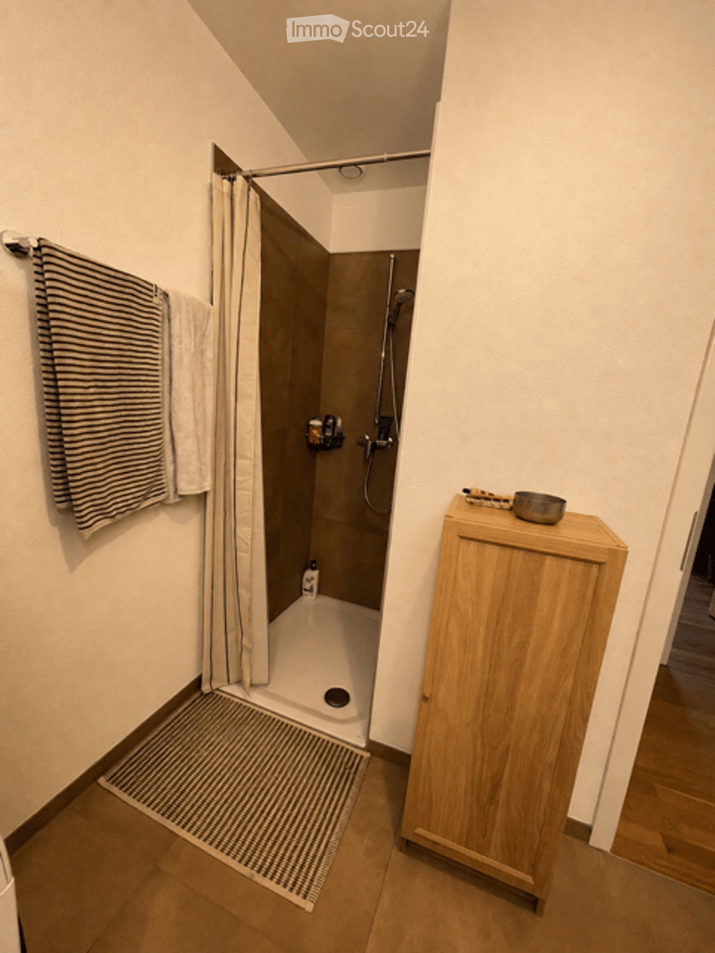 Modern bathroom with a walk-in shower, wooden cabinet, and towel hanging on the wall.
