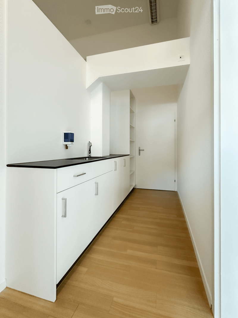 Empty room with white walls, wooden floor, white cabinets, and a sink area.