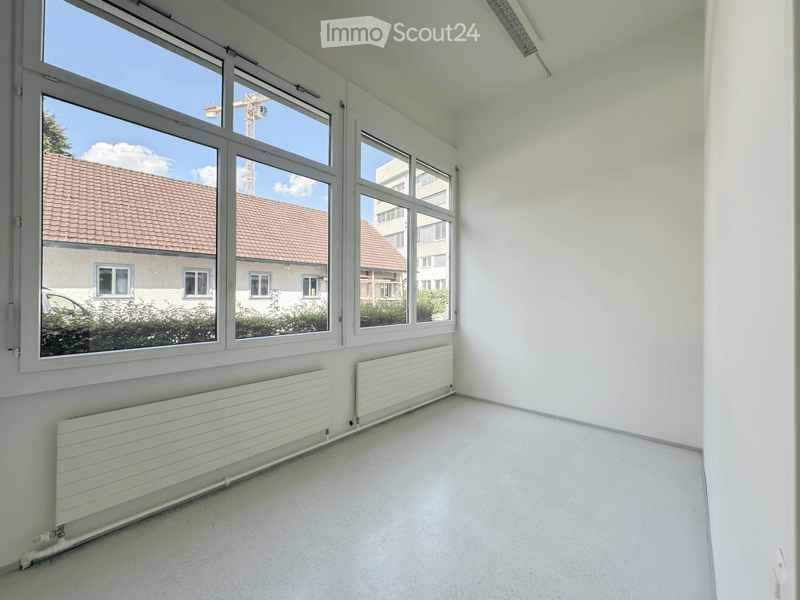 Empty room with white walls, tiled floor, large windows, and radiators along the walls.