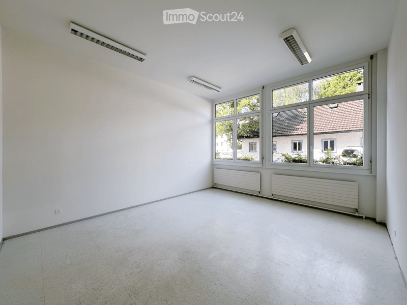 Empty room with white walls, tiled floor, large windows, and radiators.