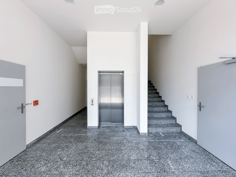 Modern, minimalist hallway with grey walls, polished stone floor, elevator, staircase, and doors.