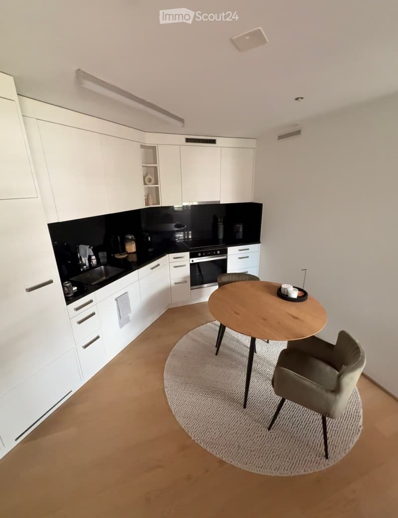 Modern kitchen with white cabinetry, black countertops, and a small dining area featuring a round wooden table and two chairs.