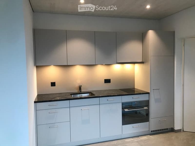 Modern kitchen with grey cabinets, a sink, and an oven, illuminated by under-cabinet lighting.