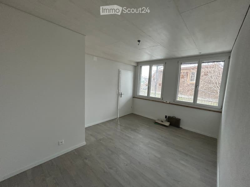 Empty room with light grey walls, wooden flooring, and large windows. No furniture or equipment present.