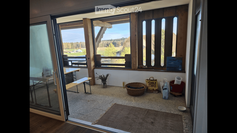 Bright, open space with large windows offering a scenic view, furnished with a table, bench, wicker basket, vase, and shopping bag.
