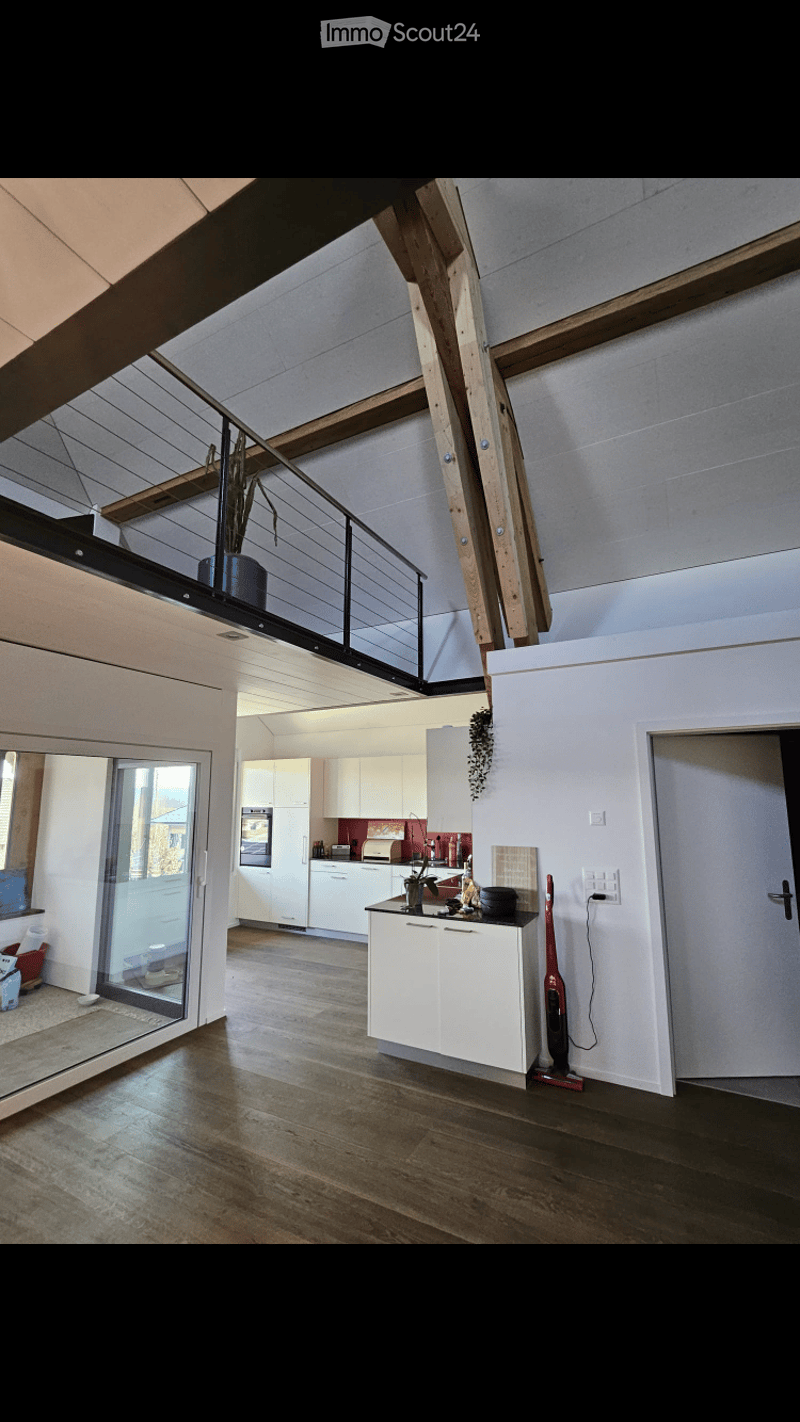 Open-plan living and kitchen area with modern white cabinets, stainless steel appliances, wooden flooring, and a sleek kitchen island.