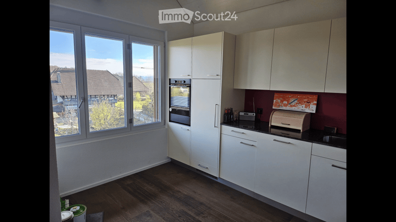 Modern kitchen with white cabinets, black countertops, and large windows offering a view of the neighborhood.