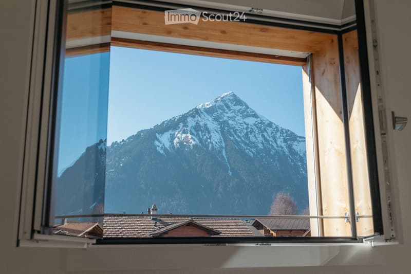 Open window with a scenic mountain view, snow-capped peaks, and a clear blue sky.