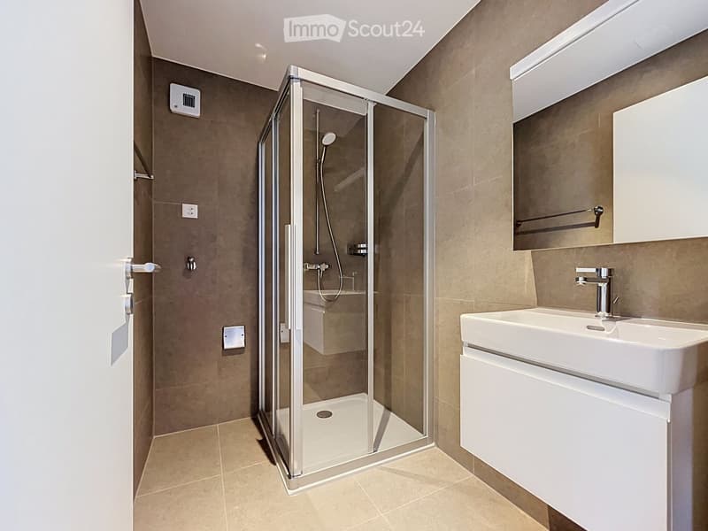 Modern bathroom with a glass-enclosed shower, a white sink with a mirror, and beige tiled walls and floor.