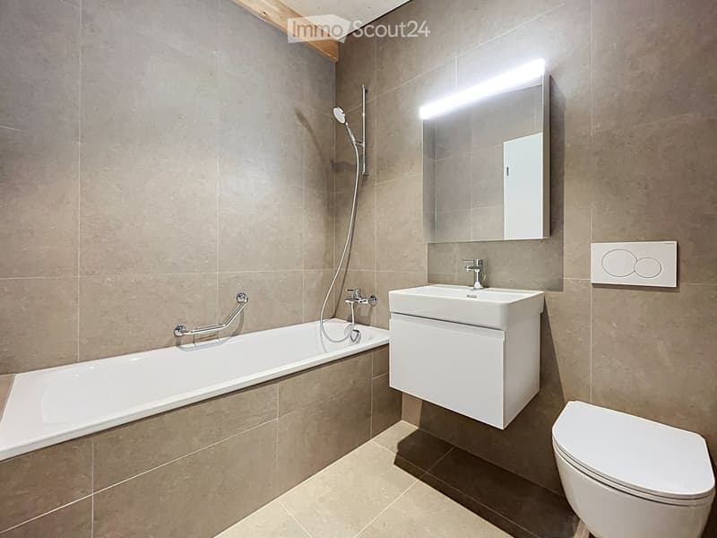 Modern bathroom with a bathtub, sink, toilet, and large mirror with built-in lighting. Beige tiles and a sleek design.