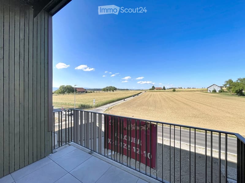 Balcony with metal railing, tiled floor, and a view of a rural landscape with fields, a road, and distant houses.