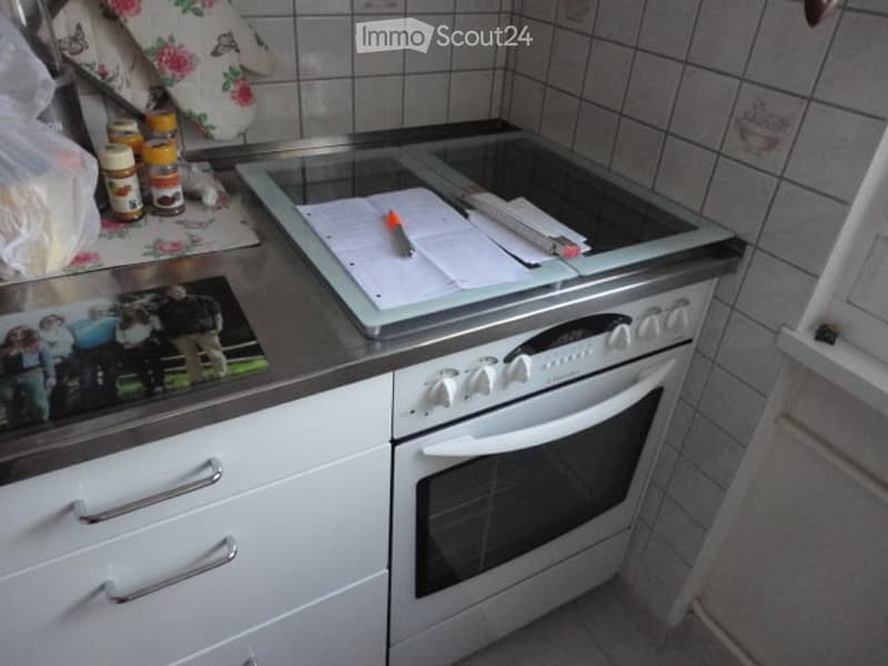 A modern kitchen with white cabinets, a built-in oven, and a stove top. The oven has a glass surface and control panel, and there are various items on the counter, including a photo frame, a plastic bag, and some jars.