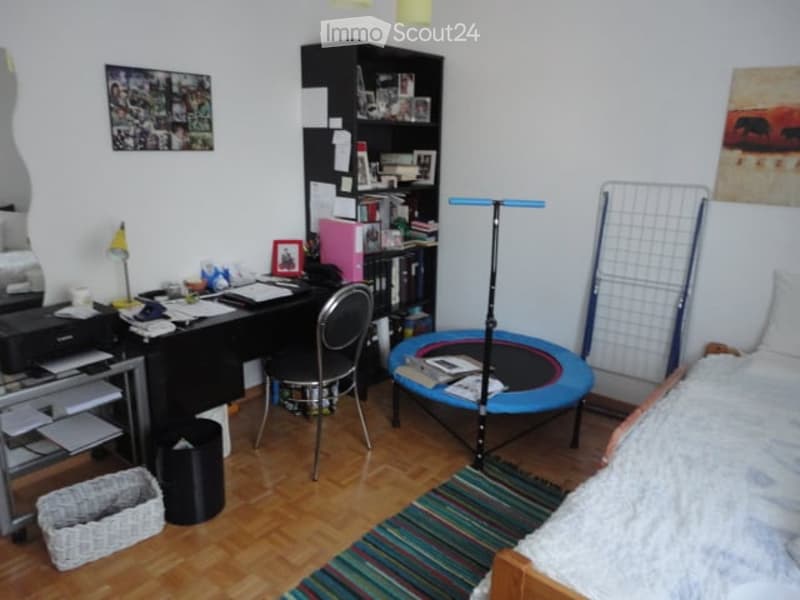 A multi-functional room with a desk, chair, bed, bookshelf, printer, lamp, mirror, picture frame, basket, and a mini trampoline.