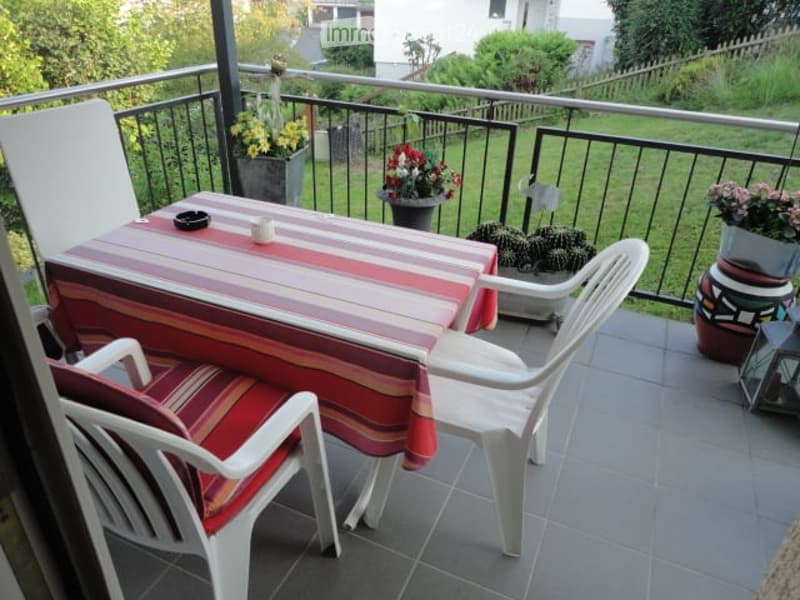 Balcony with a table, chairs, and potted plants, overlooking a green garden.