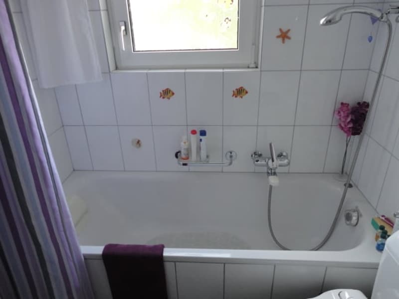 Bathtub with a showerhead and faucet, a towel on the side, and a bottle on the shelf.