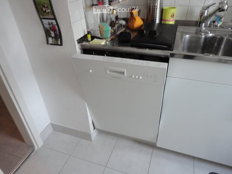 A compact kitchen with a white dishwasher, a stainless steel sink, a stove, and various kitchen items on the counter.