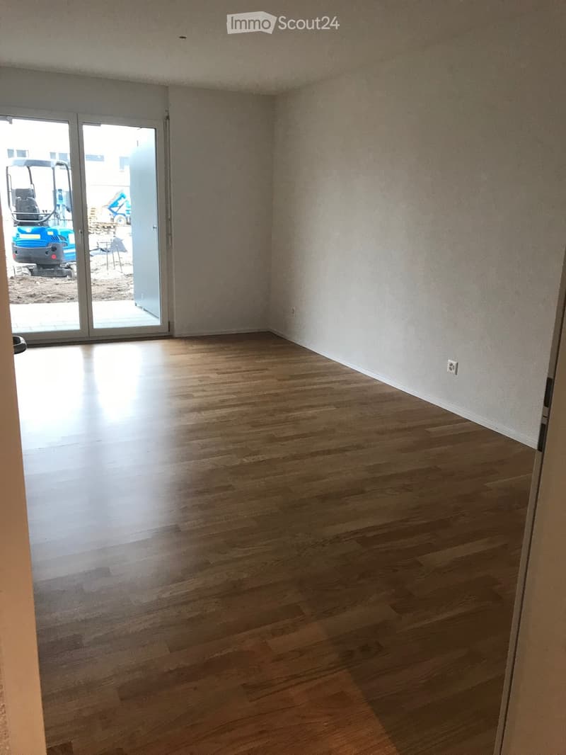 Empty room with wooden flooring and white walls, featuring a large sliding glass door leading outside.