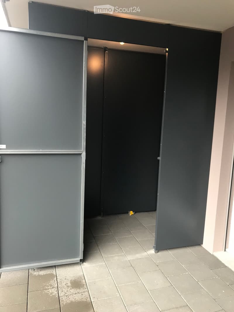 Empty hallway with tiled floor, grey walls, and a closed door at the end.