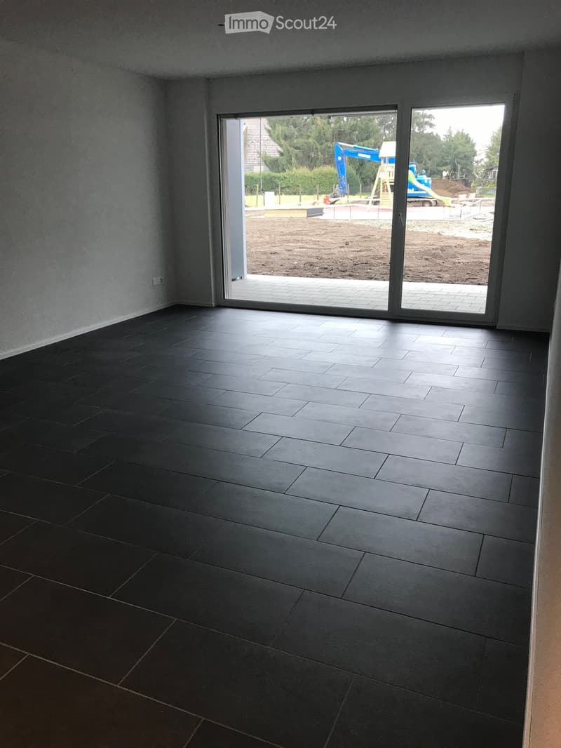 Empty room with dark grey tiled floor and large sliding glass doors leading to an outdoor area with construction equipment and playground visible.