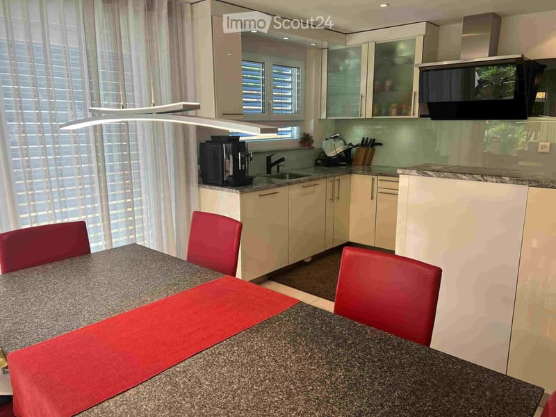 Modern kitchen with white cabinets, granite countertops, a dining table with red chairs, and a coffee machine on the counter.