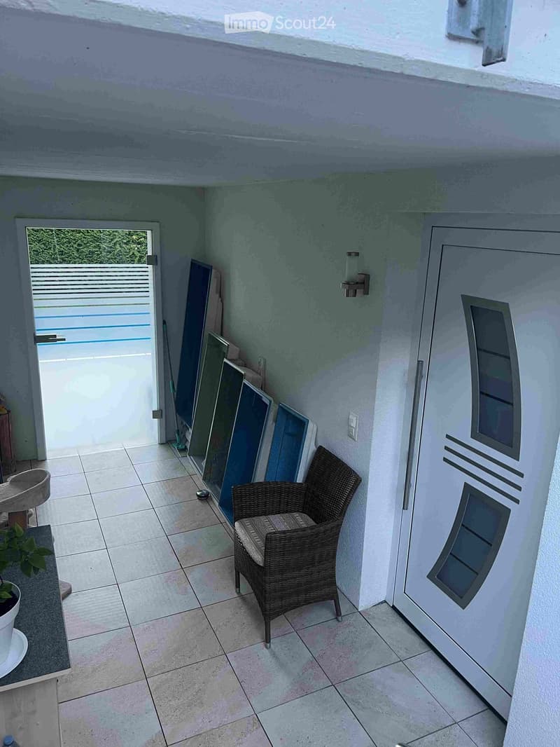 A small, tiled balcony with a wicker chair, small table, and potted plant. An open door leads to a pool area.