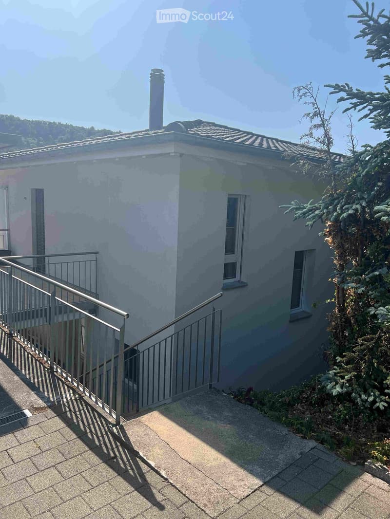 Balcony with metal railing, tiled floor, and view of a house with a chimney and windows.