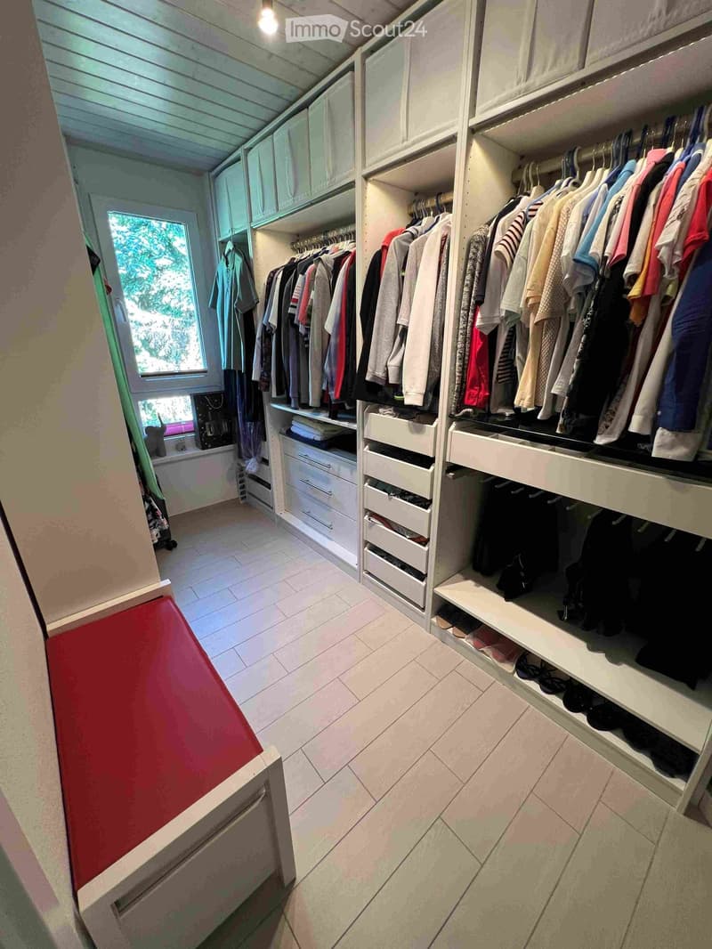 Well-organized walk-in closet with white built-in wardrobe, multiple hanging rods, drawers, and shelves filled with neatly arranged clothing and accessories.