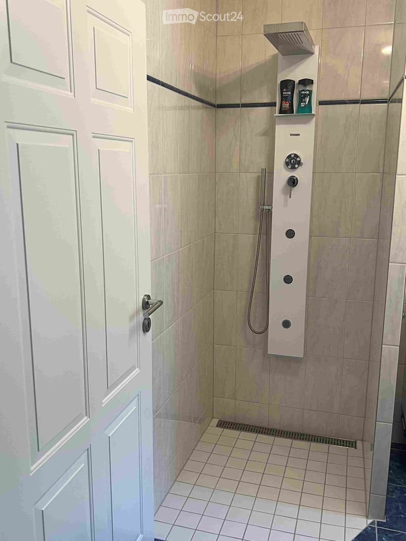 Modern shower stall with beige tiles, a control panel, and a shower bottle on a shelf.