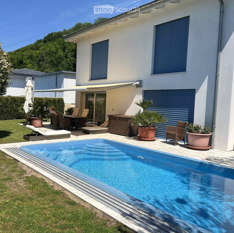Modern outdoor area with a swimming pool, patio furniture, lounge chairs, and potted plants near a house with large windows and a covered patio.