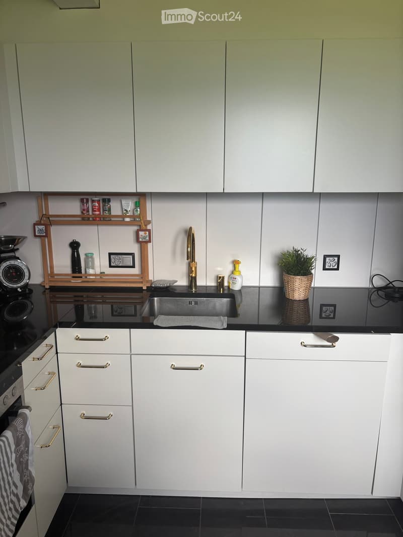 Modern kitchen with white cabinets, stainless steel sink, gold faucet, and various small appliances and decor items on the counter.