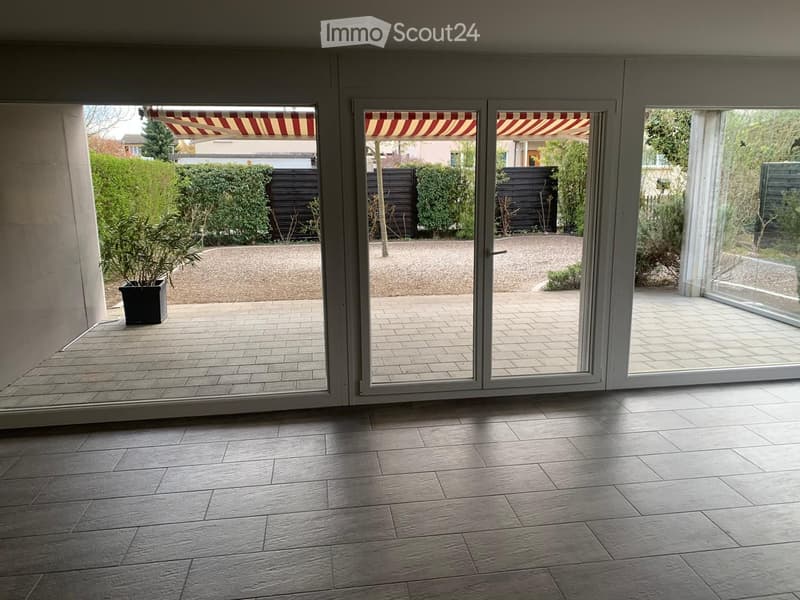 Spacious balcony with large sliding glass doors, tiled floor, and a small potted plant visible near the entrance.