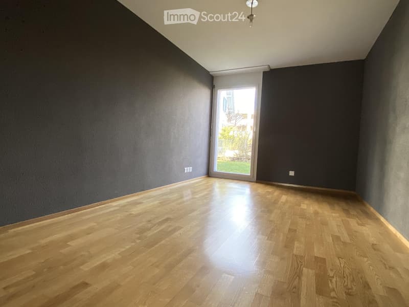 Empty room with wooden flooring, dark grey walls, and a large window letting in natural light.