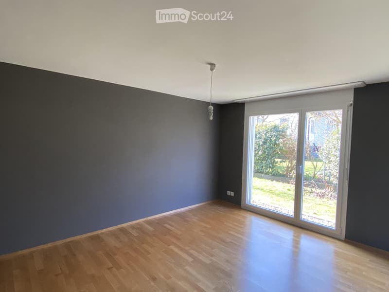 Empty room with wooden flooring, dark walls, and large sliding glass doors leading to a garden.
