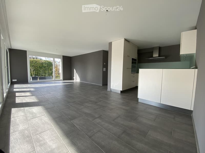 Modern kitchen with white cabinets, dark grey tiled floor, large windows, and a built-in oven and range hood.