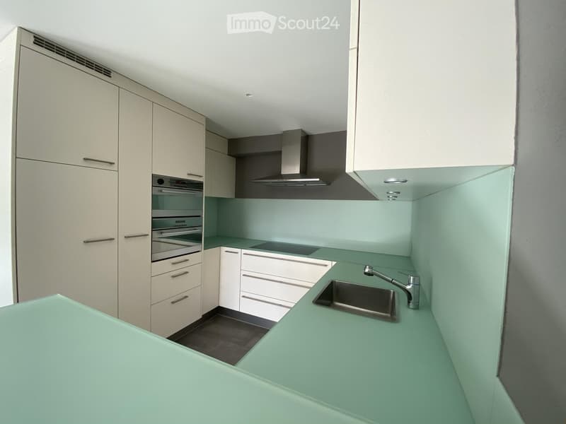 Modern kitchen with light-colored cabinets, stainless steel appliances, and a green countertop.