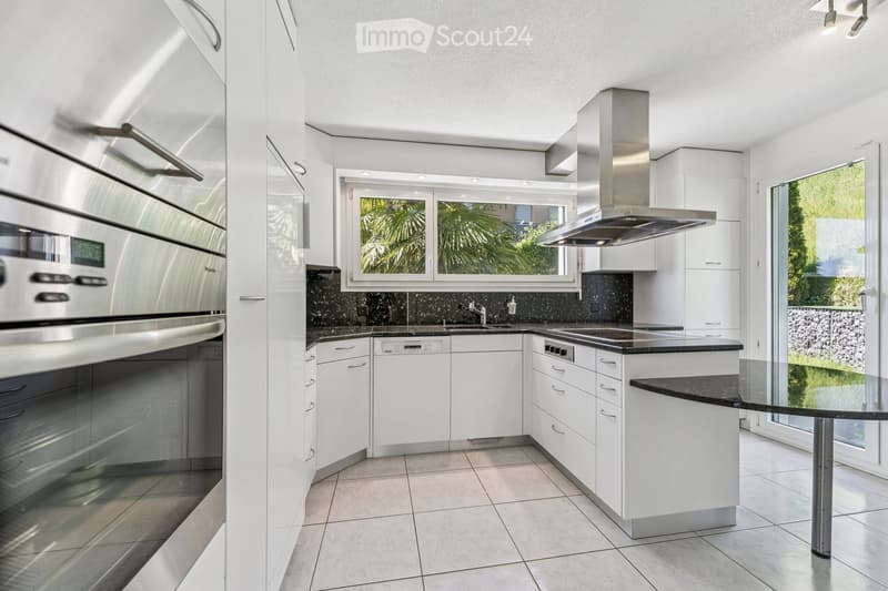 Modern kitchen with white cabinets, stainless steel appliances, black granite countertops, and large windows overlooking a garden.