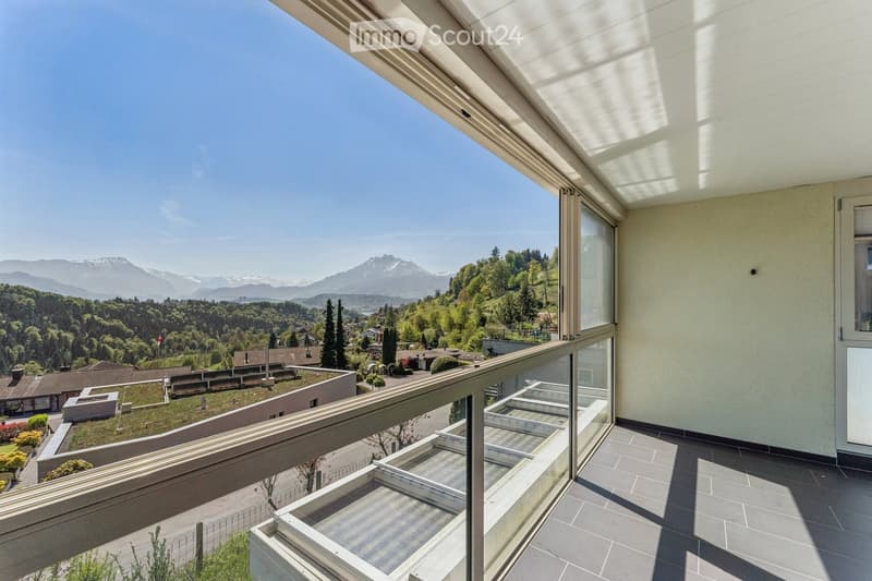Balcony with expansive mountain view, modern glass railing, tiled floor, and surrounding greenery.