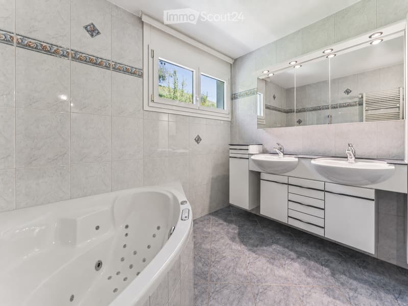 Modern bathroom with a large bathtub, double sink vanity, large mirror, and decorative tiles.