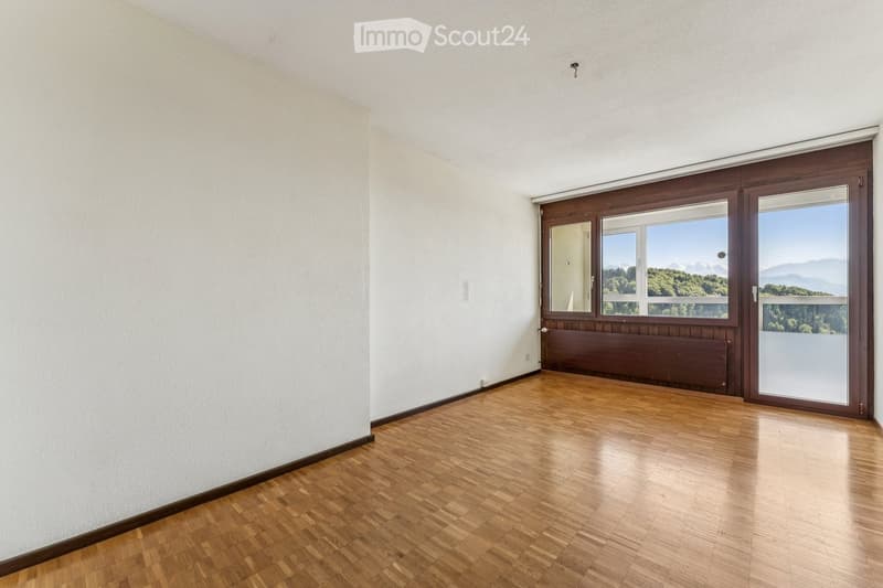 Empty room with wooden flooring, white walls, large window with wooden frame, and a radiator below the window.