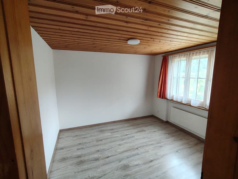 Unfurnished Room. Empty room with wooden floor, white walls, and a window with curtains. The ceiling is wooden with a built-in light fixture.