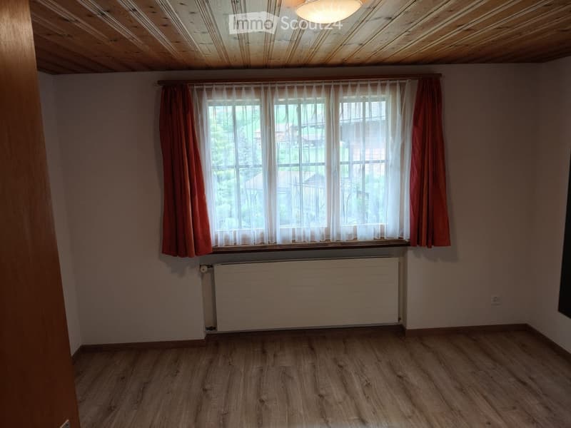 Unfurnished Room. Empty room with wooden flooring, large window with curtains, radiator, and exposed wooden ceiling beams.