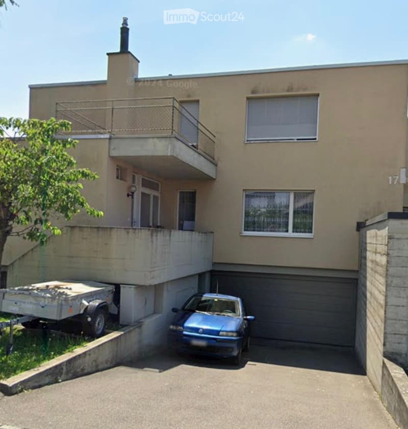 Two-story building with a balcony, garage, and a trailer parked nearby.