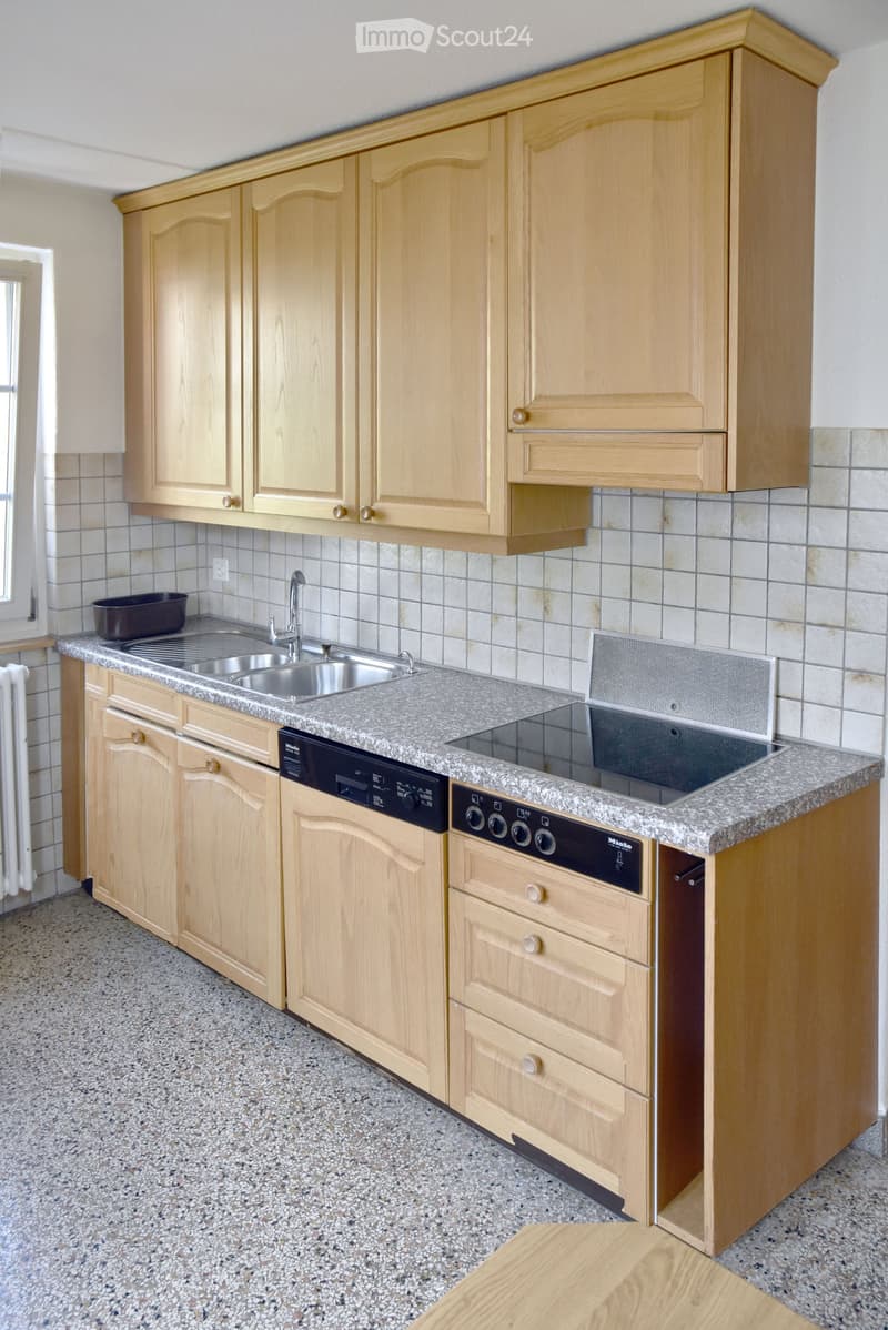 Modern kitchen with light wooden cabinets, granite countertop, stainless steel sink, oven, and dishwasher.