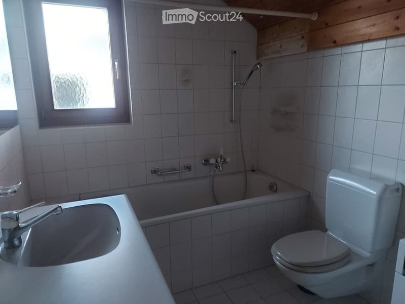 Bathroom with a bathtub, toilet, sink, and showerhead. The room has tiled walls and a window providing natural light.
